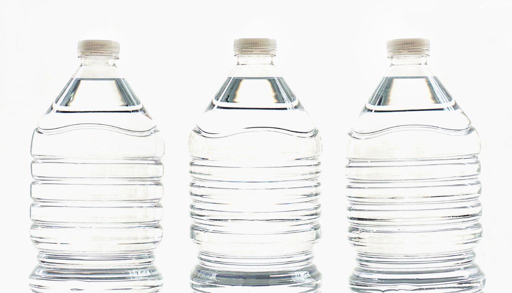 Photo of three full plastic water bottles in front of white background created by the blow molding process